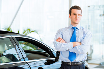 dealer stands near a new car in the showroom