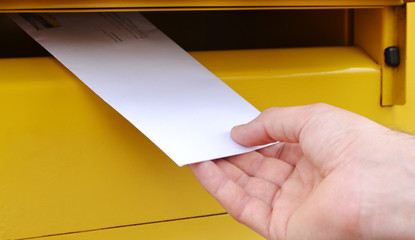 Menschliche Hand haltet einen Brief vor der gelben Briefkasten.. Postsendung in Deutschland.