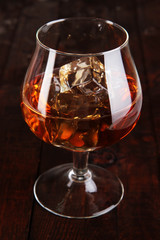 Brandy glass with ice on wooden background