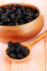 Ripe mulberries in bowl and spoon on wooden background