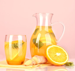 Orange lemonade in pitcher and glass on pink background