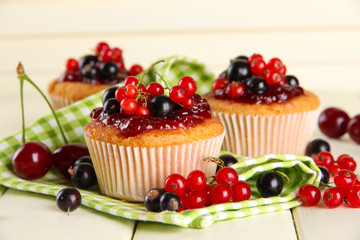 Tasty muffins with berries on white wooden table