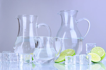Glass pitchers of water with ice and lime on grey background
