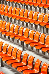 Plenty of orange  plastic seats at stadium .