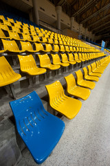 One of blue in plenty of yellow plastic seats at stadium .