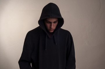 teenager with hoodie looking down against a dirty gray wall