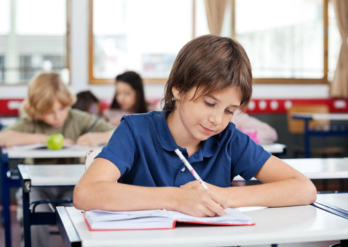 Schoolboy Writing In Book At Desk - Powered by Adobe