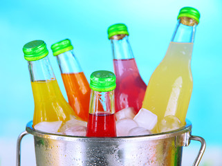 Bottles with tasty drinks in bucket with ice cubes, in bright