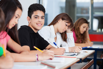 Teenage Boy Sitting With Friends Writing At Desk