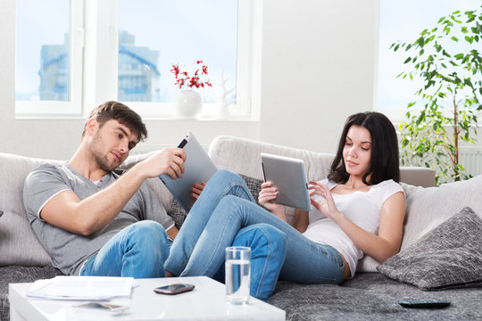 couple sitting on a couch with tablet computers