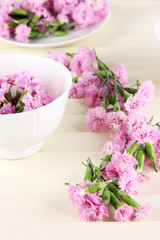 Many small pink cloves in cup and on saucer on wooden