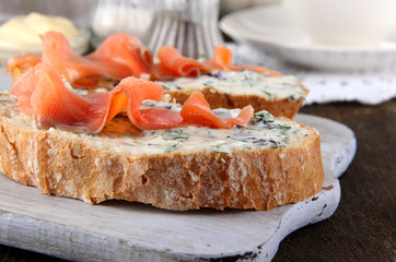 Fish sandwiches and cup of tea on cutting board on wooden table