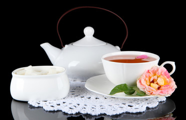 Kettle and cup of tea from tea rose on napkin black background
