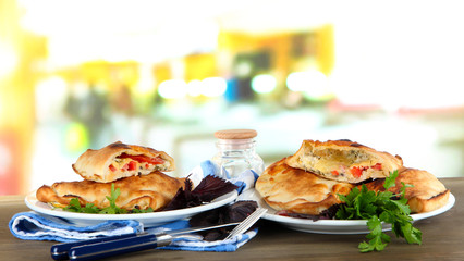 Pizza calzones on plates on table on room background