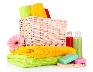 Colorful towels in basket, cosmetics bottles and soap, isolated
