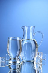 Glass pitcher of water and glass on blue background