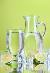 Glass pitcher of water and glass on green background