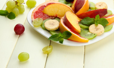 Assortment of sliced fruits on plate, on white wooden table