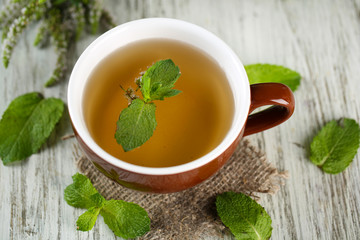 Cup of herbal tea with fresh mint flowers on wooden table