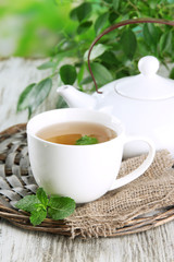 Teapot and cup of herbal tea with fresh mint on wooden table