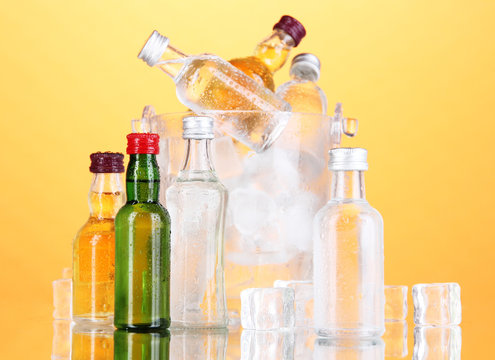 Minibar bottles in bucket with ice cubes,  on color background