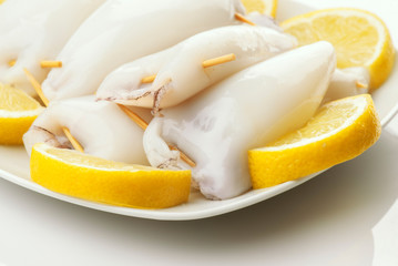 raw squid stuffed ready to be cooked in plate and cut lemons