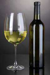 White wine glass and bottle of wine on grey background