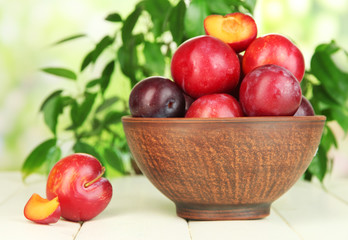 Ripe plums in bowl on wooden table on natural background