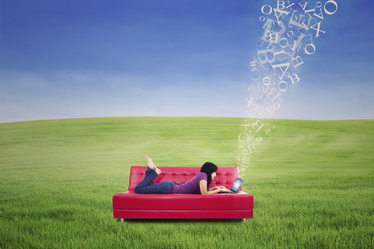 Attractive female lying on red sofa and typing e-mail outdoor