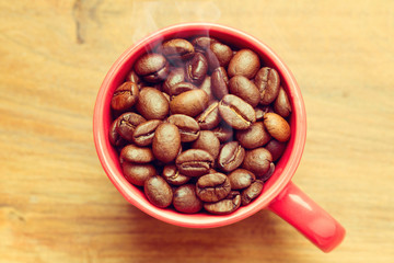 Coffee beans in red cup over wooden background
