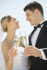 Couple Toasting Champagne Flutes Against Sky