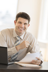 Businessman With Documents And Pen Sitting At Desk