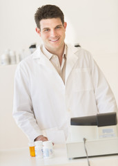 Pharmacist Smiling While Standing At Counter In Drug Store