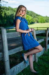 Young pretty blonde posing in summer field near a fence