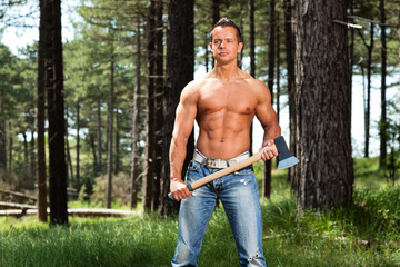 Shirtless muscled fitness lumberjack man with axe in forest.