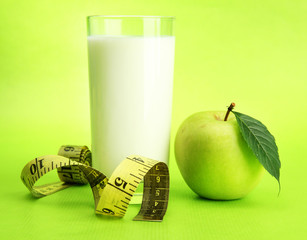 Glass of kefir, apple and measuring tape, on green background