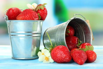 Ripe sweet strawberries in metal pails on blue wooden table