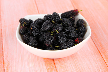 Ripe mulberries in bowl on wooden background