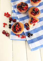 Tasty muffins with berries on white wooden table