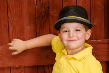 Portrait of child wearing fedora hat next to rustic barn