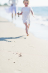 Closeup on sand and mother and baby running along sea shore
