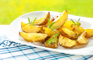 Baked wedges potatoes with rosemary on white plate