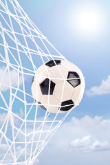 Soccer ball in a net against cloudy sky