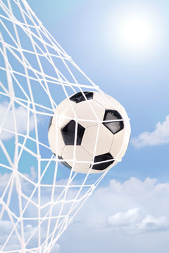 Soccer ball in a net against cloudy sky