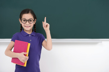 Smart little girl. Pretty little schoolgirl holding her finger u