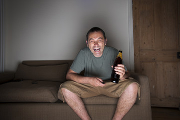 man drinking beer and laughing at the tv