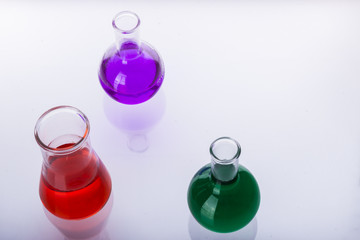 Laboratory glassware with liquids of different colors on white b
