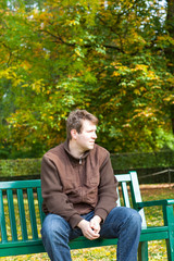 young man in the autumn park sitting on bench