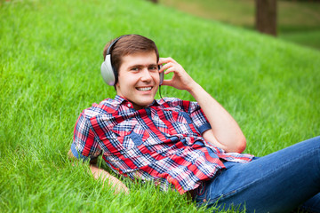 Handsome young man with headphones at green grass