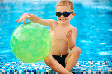 Cute boy in sunglasses sitting at pool